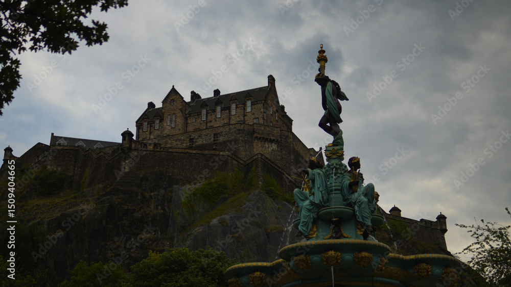 Obraz premium The Edinburgh Castle perched on a cliff seen from a fountain in Scotland, UK