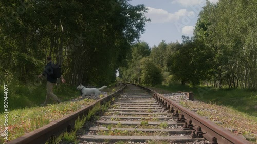 A man with his dog is crossing the railway tracks, walking to the other side