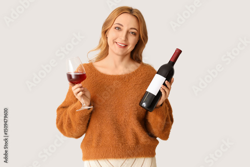 Beautiful mature woman with glass and bottle of wine on white background