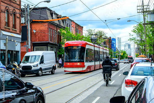 public transport: modern tram car  and food delivery bike courrier on city street shot in the queen west area of toronto on a sunny spring day 
