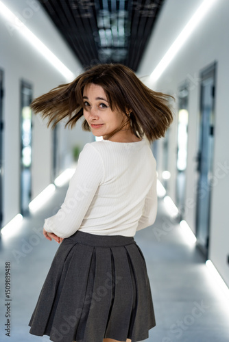 Young woman twirling in a modern hallway. A young woman with brown hair smiles playfully while twirling in a brightly lit hallway with minimalistic decor. Free Download Young woman twirling in a modern hallway. A young woman with brown hair smiles playfully while twirling in a brightly lit hallway with minimalistic decor. - GFXLoad