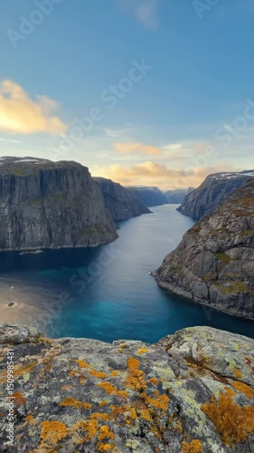 sunset over deep nordic fjord with steep rocky cliffs and vivid orange moss on foreground boulders warm sky reflected in still blue water concept of outdoor travel, tourism branding, luxury retreats
