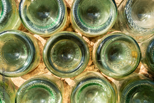 The bottoms of green bottles are photographed from above. The image captures the circular shapes and textured patterns of the glass