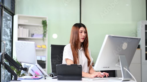 Asian woman working on desktop computer in bright office. Ideal for business, digital marketing, productivity, modern workplace, and corporate concept