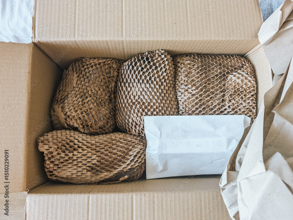 Obraz premium Cardboard box containing wrapped items with protective paper and packaging material, top view.