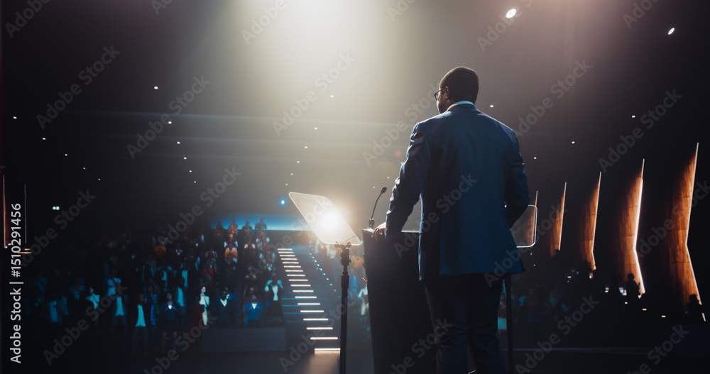 © Gorodenkoff - Confident Thought Leader Walking to a Tribune with laptop Computer, Delivering an Inspiring Presentation About Innovation at Technology Conference. Black Man Talking to an Audience in a Dark Venue