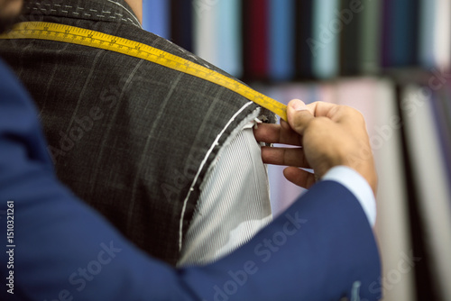Close-up of bespoke tailor taking measurements of client for a suit with yellow measurements tape