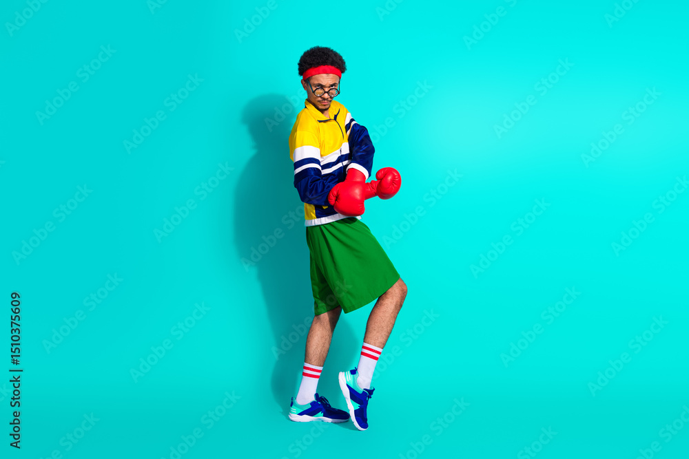 Fototapeta premium Energetic young man posing in retro activewear on teal background, boxer gloves