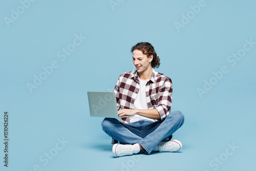 Принти на полотні Full body young IT man he wearing purple checkered shirt casual clothes sits hold use work on laptop pc computer isolated on plain pastel light blue cyan background studio portrait