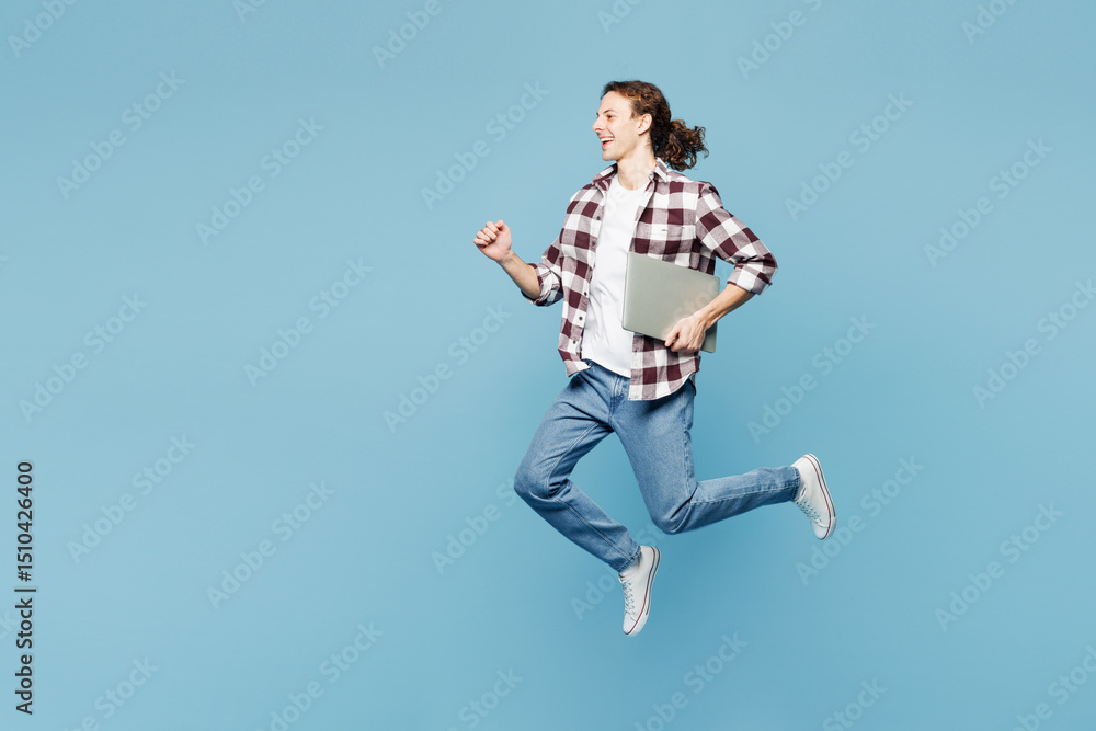 Full body young IT man wear purple checkered shirt casual clothes jump high hold use work on laptop pc computer isolated on plain pastel light blue cyan background studio portrait. Lifestyle concept. Full body young IT man wear purple checkered shirt casual clothes jump high hold use work on laptop pc computer isolated on plain pastel light blue cyan background studio portrait. Lifestyle concept.