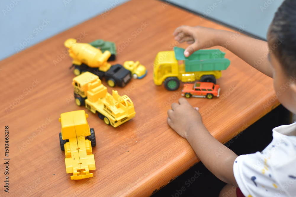 Obraz premium 3 year old boy playing with toy cars on wooden table