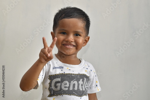 close up of 3 year old boy raising two fingers while smiling, on white background