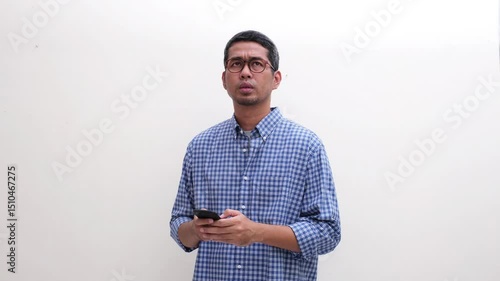 Adult Asian man showing serious expression when texting on his mobile phone