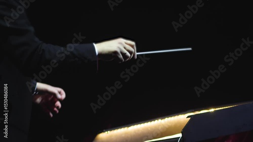 Male conductor behind the podium directing orchestra on stage with pupitre, musicians and choir, the philharmonic venue hall during concert, symphony orchestra director hands conducting waving baton