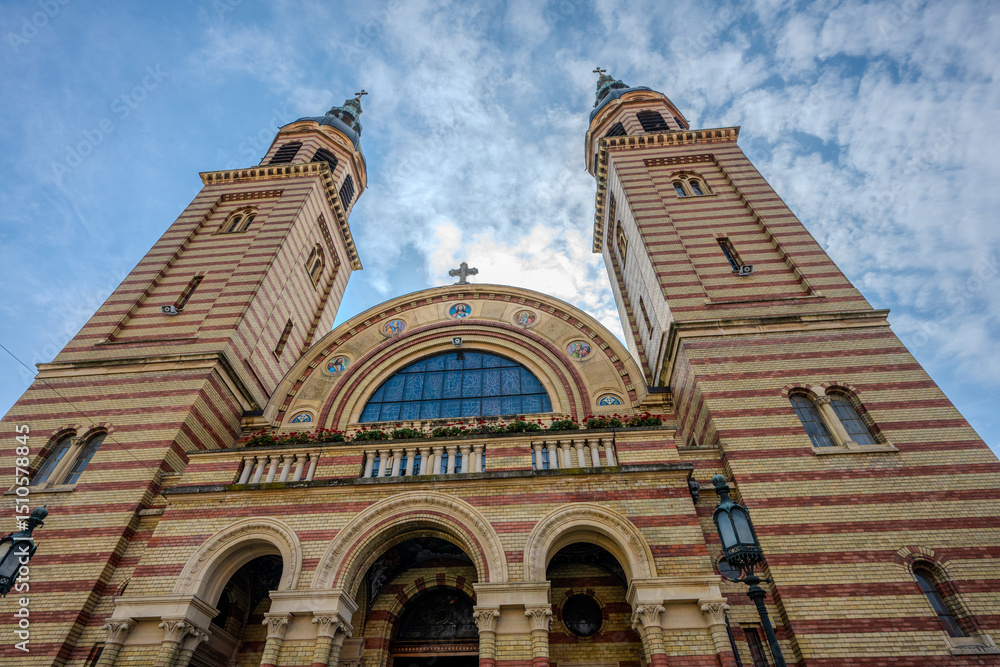 Fototapeta premium Low Angle View of the Holy Trinity Roman Catholic Church in Sibiu, Romania with Neo-Romanesque Architecture and Twin Bell Towers Against a Dramatic Sky