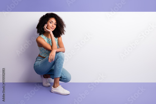 Fototapeta Trendy young woman in casual outfit seated against vibrant purple background, sh