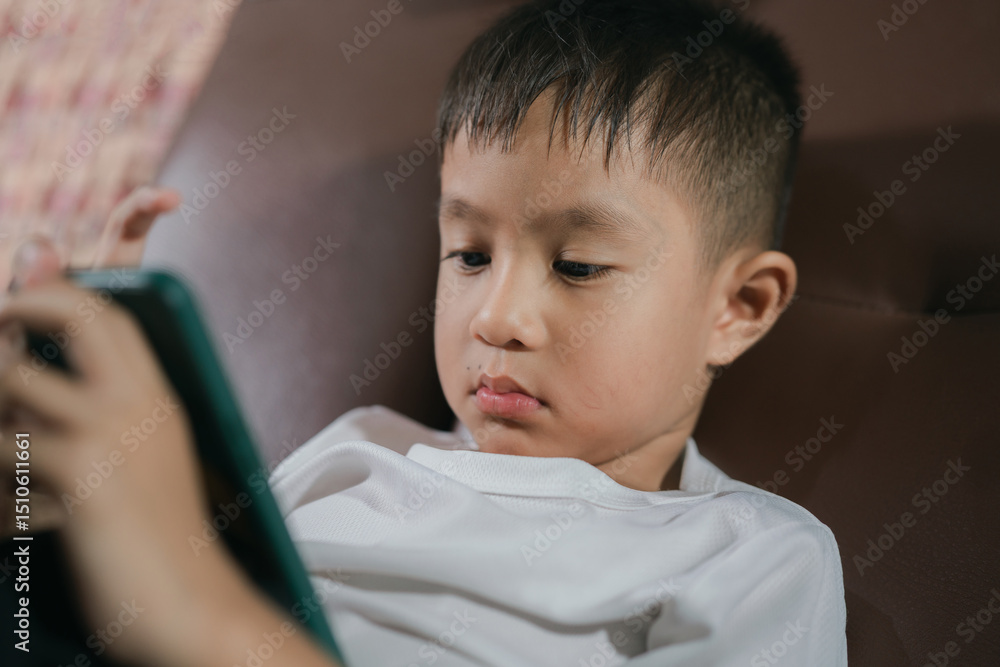 Cute little boy watching videos,relaxing at home.little boy lying down looking at the phone, close-up. little boy use of smart phone and lying down on sofa Cute little boy watching videos,relaxing at home.little boy lying down looking at the phone, close-up. little boy use of smart phone and lying down on sofa