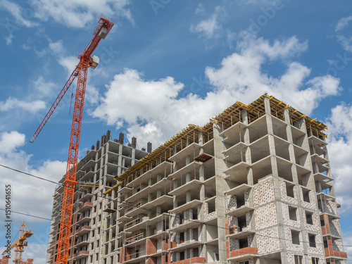 A tower construction crane at a construction site. The frame of a building under construction. The structure of the building. Load-bearing reinforced concrete walls of the house.
