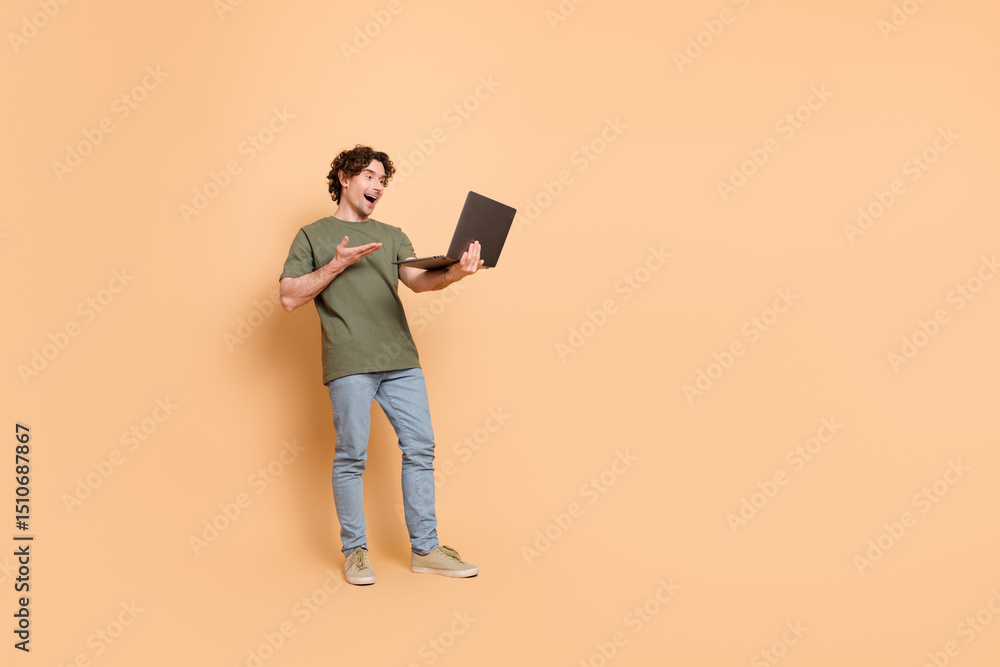 Happy young man with curly hair enjoying online interaction on a laptop against a beige background Happy young man with curly hair enjoying online interaction on a laptop against a beige background