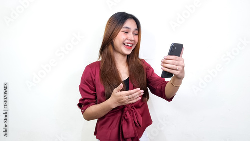 Foto Beautiful Asian woman wearing red blouse looking at smartphone with happy interested face, isolated on white background