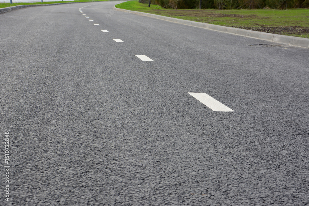 Obraz premium Curving asphalt road with white lane markings close up