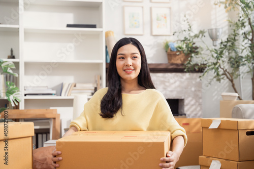 Asian smiling woman with cardboard boxes for moving to the new home. Concept of people moving house, buying property and decorating room