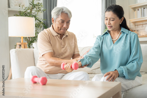 Asian senior couple exercise with lifting dumbbell for strength training on couch together at home. Healthy lifestyle people insurance concept.