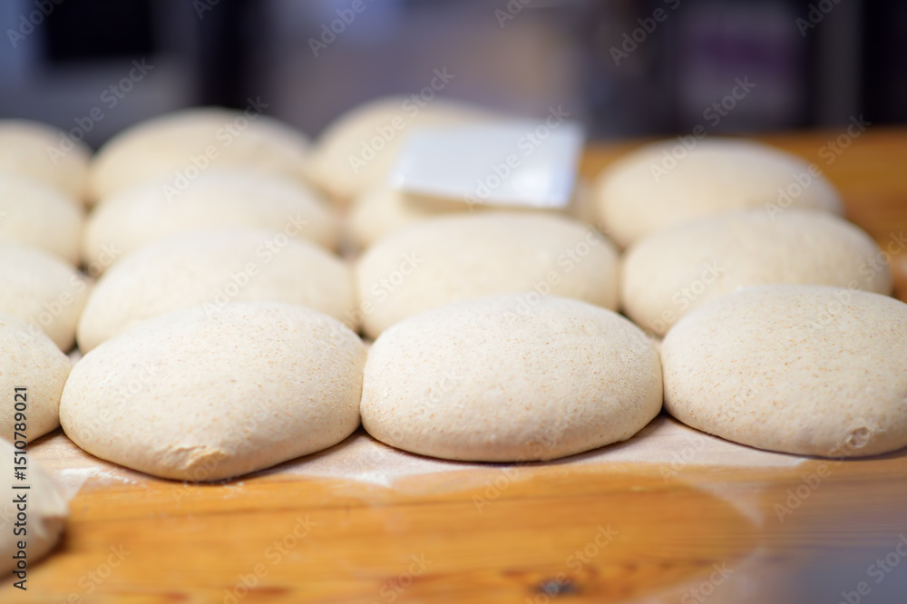 A batch of formed dough pieces on a table in the kitchen of a local bakery ready to bake. Olive ciabatta blanks laid out in a row in front of a large oven. Local bread production A batch of formed dough pieces on a table in the kitchen of a local bakery ready to bake. Olive ciabatta blanks laid out in a row in front of a large oven. Local bread production