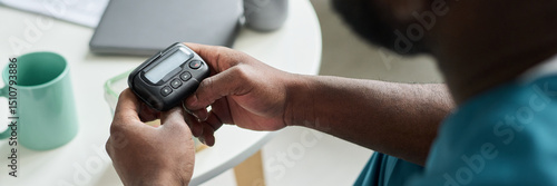 Person holding pager with both hands while sitting at table with cup and laptop in background, focused on device