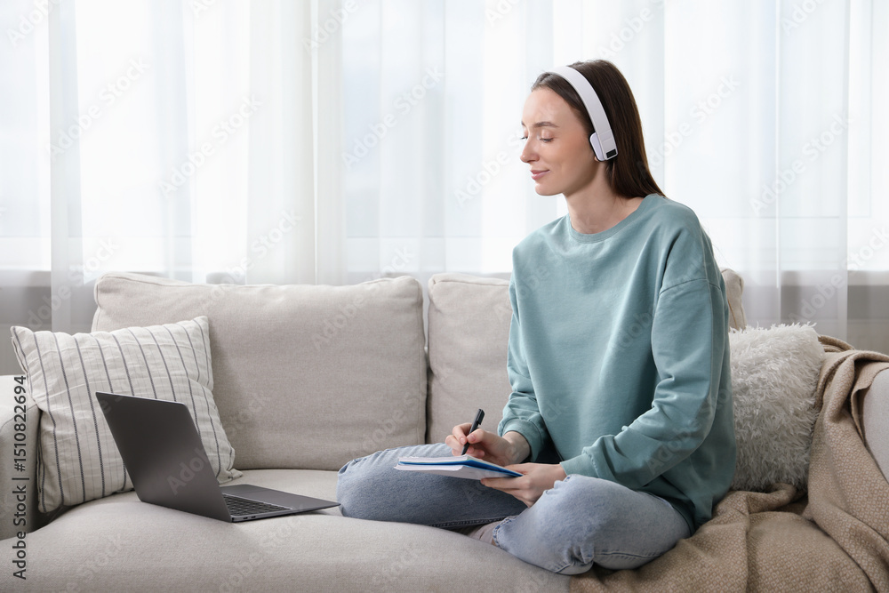 Woman taking notes during online lesson on sofa indoors. Self-study Woman taking notes during online lesson on sofa indoors. Self-study