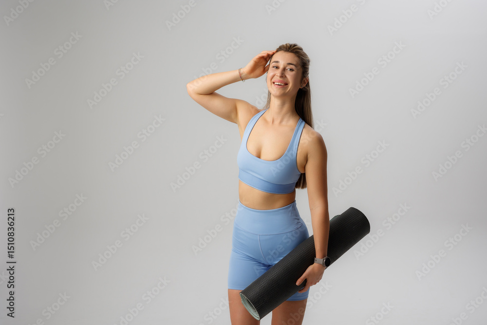 Obraz premium Woman in blue workout attire holding yoga mat in a studio setting during a fitness session