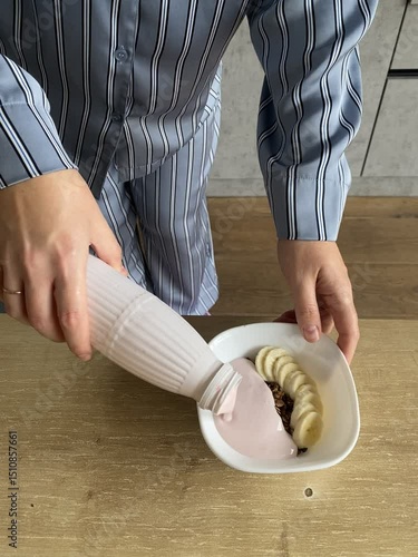 young woman pours yogurt into a plate with granola and bananas, breakfast concept