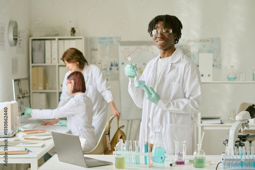 Student working with lab equipment, performing experiment. Two colleagues working on research in background. Laboratory setting with scientific tools and samples Student working with lab equipment, performing experiment. Two colleagues working on research in background. Laboratory setting with scientific tools and samples