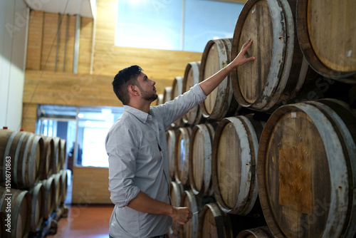 Professional man winemaker working and inspecting wine quality in cellar with wooden barrel in factory. Winery manufacturing industry, Alcohol and winemaking fermentation process.