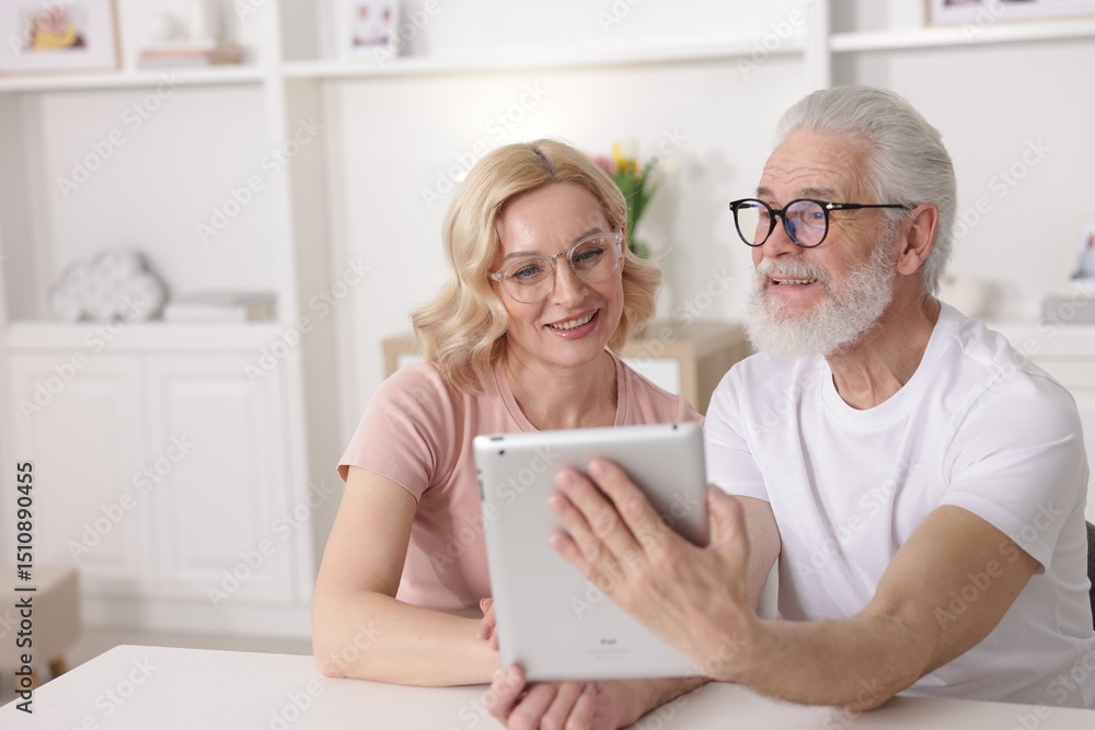 Senior man and mature woman watching something on tablet at home. Happy couple Senior man and mature woman watching something on tablet at home. Happy couple