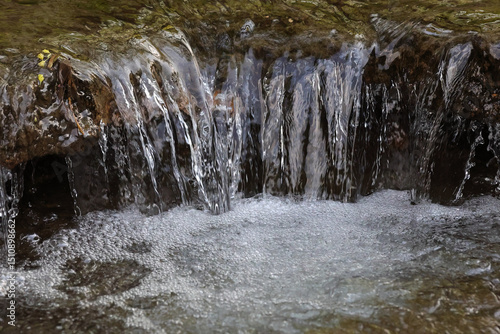 Macro Close Up Of A Small Natural Waterfall With Clear Water Flowing Over Rocks, Creating White Bubbles And Foam.