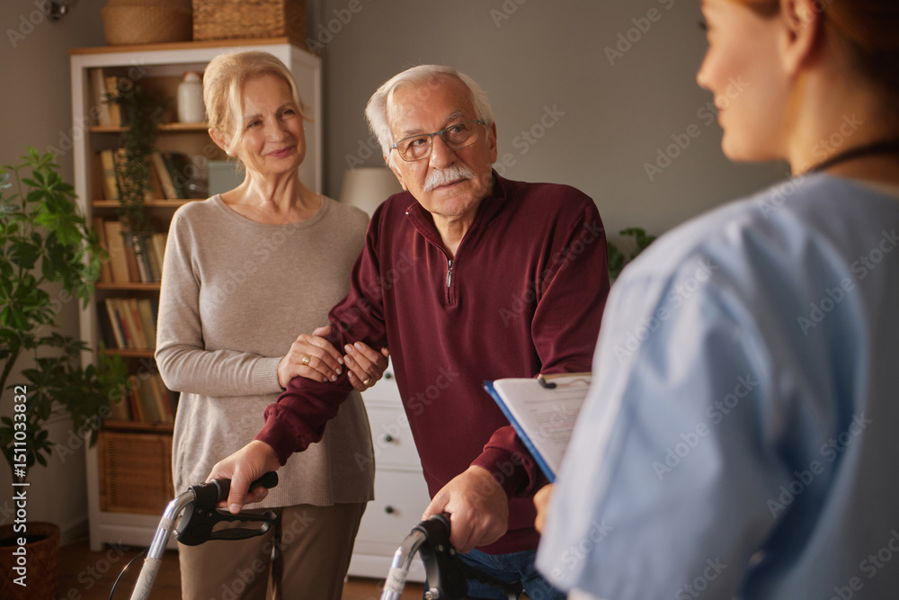 Fototapeta premium A elderly man with a walker receives medical advice from a professional while being supported by a woman in a comfortable living space filled with plants.