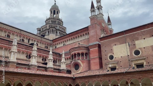 View of the Certosa di Pavia ornate red brick monastery and bell tower from the inner courtyard, showcasing Renaissance and Gothic architectural details under a cloudy sky