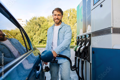 Schilderij op canvas Happy European man refueling car at gas station, standing near automobile and ho