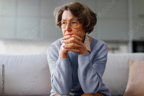 Cuadro en lienzo Depressed senior lady touching chin, sitting on sofa and looking away, feeling w
