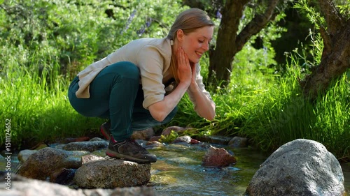 Beautiful young woman washing from mountain stream on summer day
