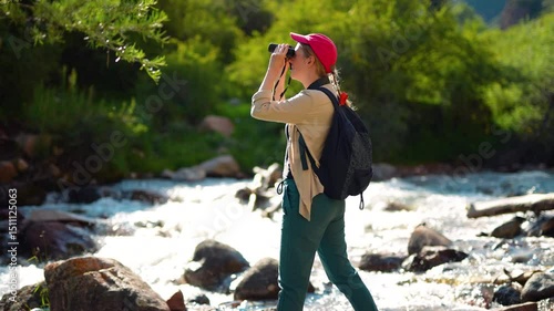 Young woman tourist with binoculars on the banks of mountain river