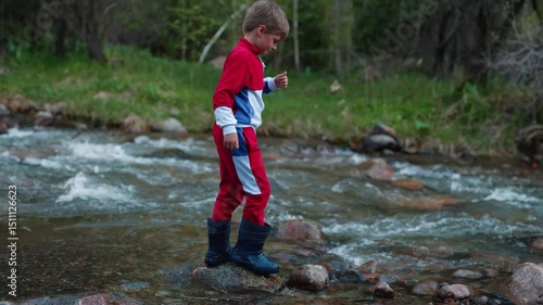 Child in boots crosses mountain river on summer day