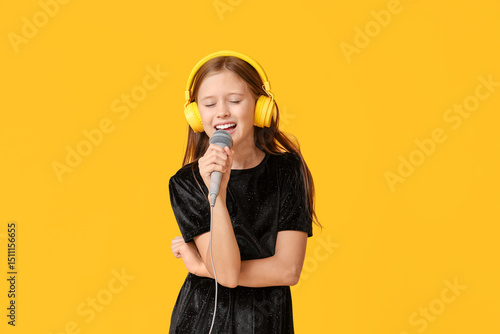 Cute girl in headphones singing with modern microphone on yellow background