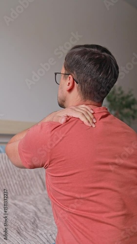 Vertical video from the back of a man suffering from pain and massaging his neck and shoulders at home, osteochondrosis, hernias and protrusions.