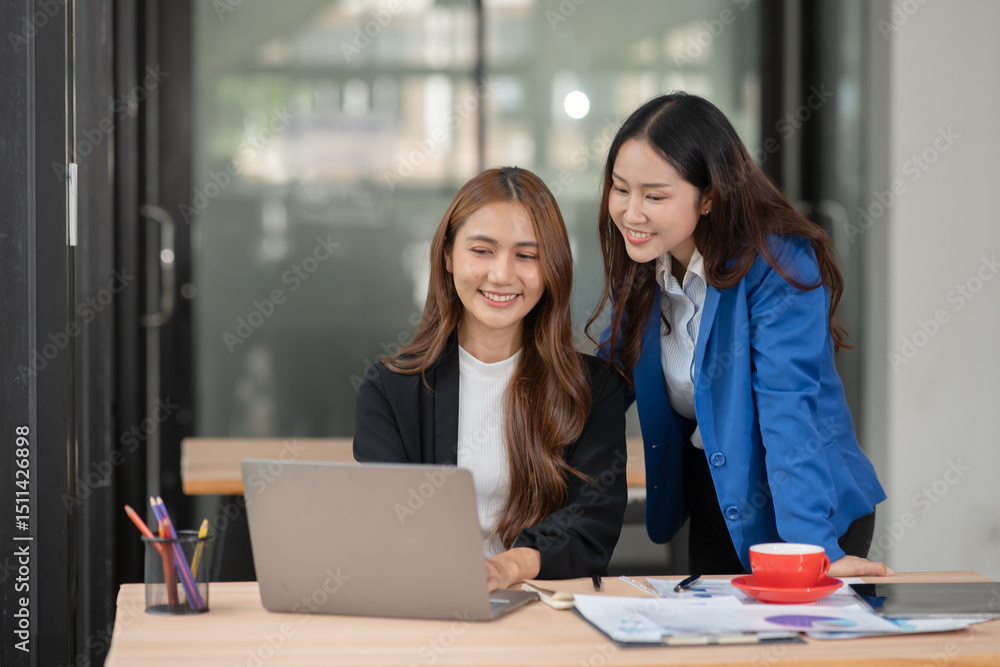 Two Asian businesswomen using laptops, on the table there are graph documents working on business investment. Two Asian businesswomen using laptops, on the table there are graph documents working on business investment.
