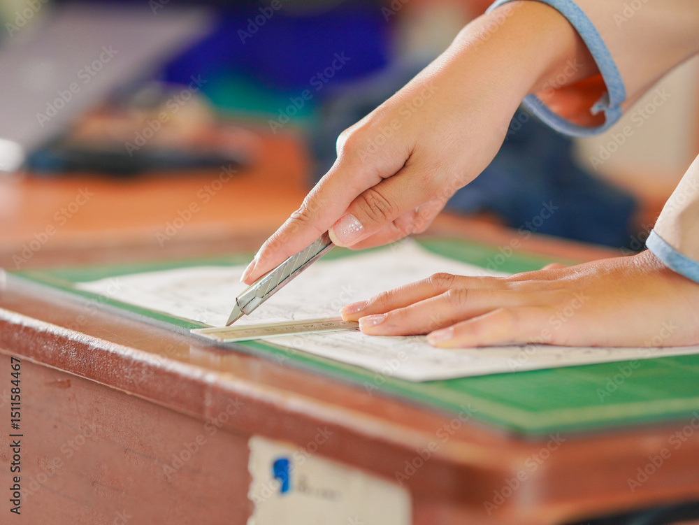 Obraz premium Closeup hand female using cutter to cut the paper in classroom at kid school. Lifestyle Concept Children's learning development and handwork or teaching students, education learning knowledge