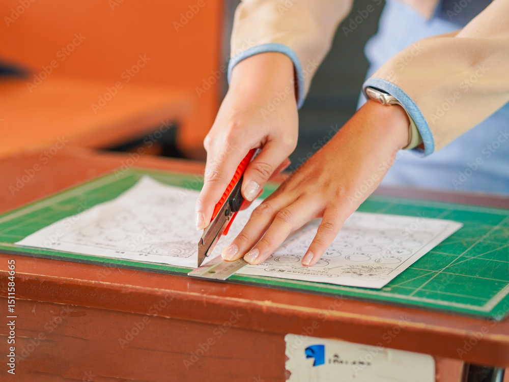 Obraz premium Closeup hand female using cutter to cut the paper in classroom at kid school. Lifestyle Concept Children's learning development and handwork or teaching students, education learning knowledge