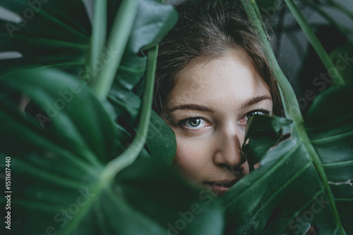woman's face is partially obscured by the lush green leaves of a plant