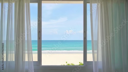 Beach view through open sliding glass door with white sheer curtains blowing in breeze, turquoise ocean, blue sky, sunny day.